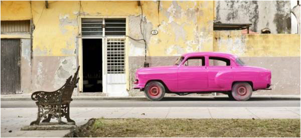 A vintage brightly painted Cuban car in front of a crumbling building