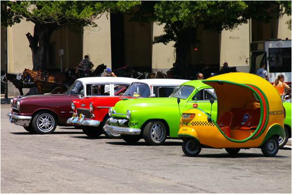 A Cuban rickshaw next to brightly painted vintage cars