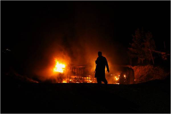 A security personnel walks past a burning passenger bus carrying Shia pilgrims at the site of a suicide car bomb attack