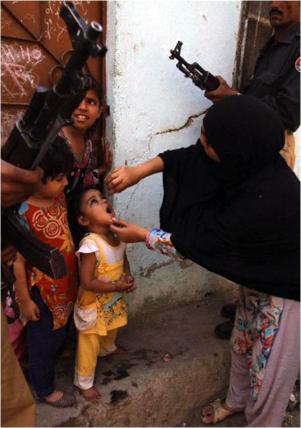 Policemen guard a health worker giving polio vaccine to a child