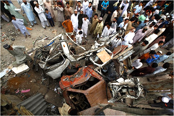 People stand near damaged vehicles at the site of a bomb explosion outside an election office of the Awami National Party (ANP) in Karachi in 2013