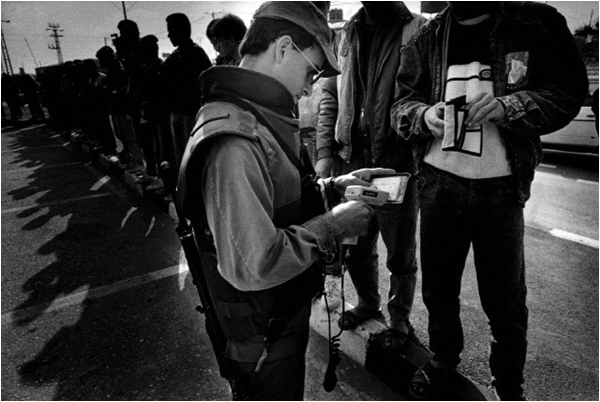 Palestinians workers wait to have their IDs checked by soldiers using barcode readers, so they can enter Israel for work