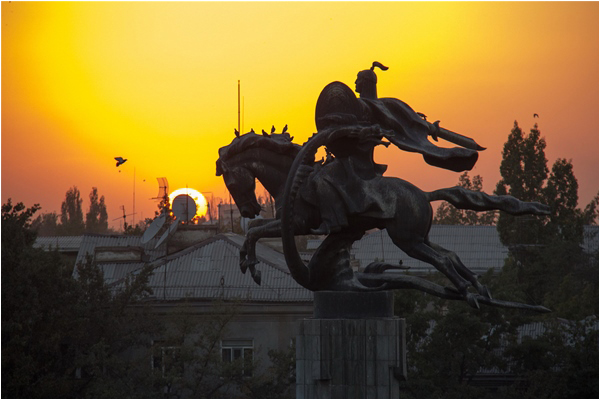 The sun sets behind a statue of epic hero Manas in Bishkek