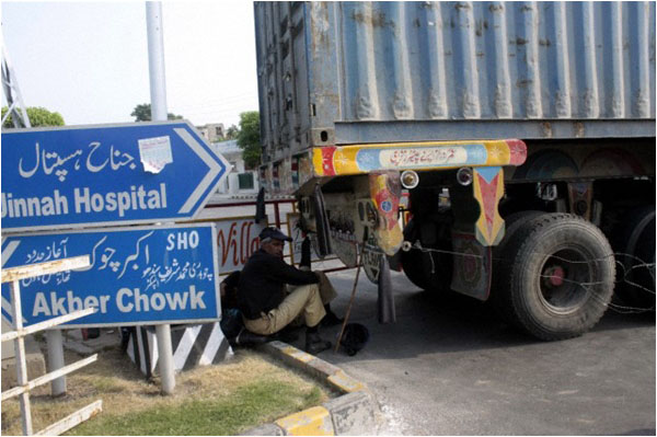 A policeman rests in the shade of a container truck placed to block the roads leading to the residence of Tahirul Qadri