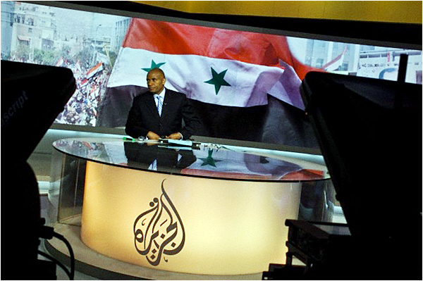 Newscaster Tony Harris, formerly of CNN, presents the afternoon headlines on Al Jazeera, with a large Syrian flag in the background