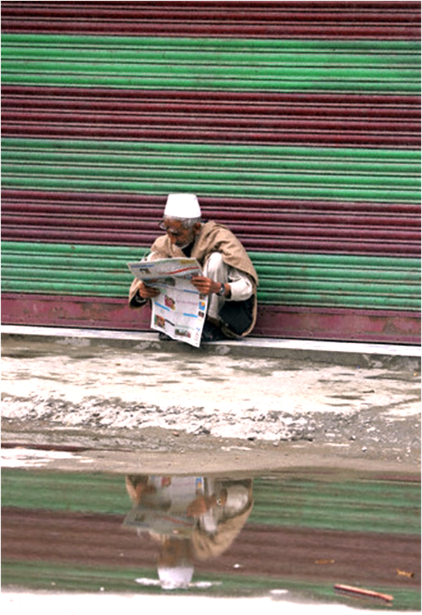 An elderly man reads a newspaper outside a closed shop during a strike in Srinagar. Veteran Kashmiri journalist and human rights defender Balraj Puri passed away on August 30