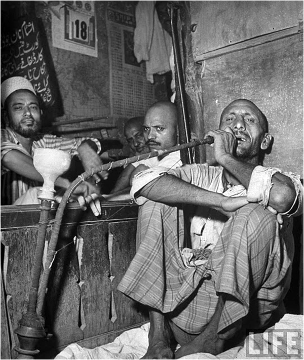 Man smoking a hooka pipe as others look on – Lahore 1946